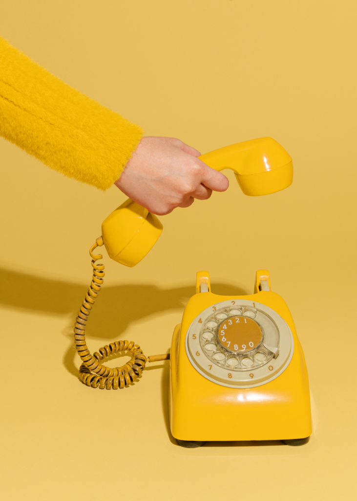 A person is holding a yellow telephone on a vivid yellow background, showcasing a playful and cohesive color theme.